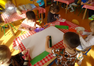 Piątka dzieci przygotowuje plakat, wycinają papierowe elementy z wycinanek.